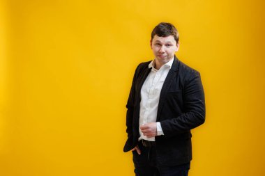 Portrait of smiling businessman wearing suit standing on yellow studio background and looking at camera