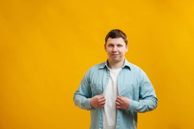 Portrait of handsome european man in shirt looking at camera standing on yellow studio background