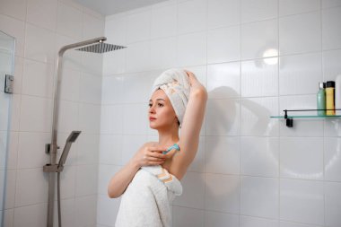 Beyaz havluyla güzel bir kadın duş kabininde koltuk altlarını jiletle tıraş ediyor. Tuvalette depolama prosedürü