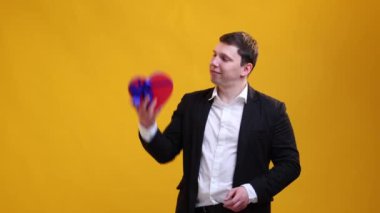 Suttisfied businessman throws St.Valentine's Day gift in heart form in the air on studio background and showing thumbs up. International Women's Day and birthday holiday concept