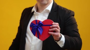 St.Valentine Günü hediyesini stüdyo arka planında heyecanlı yüz ifadesi olan kadınlara kalp şeklinde sunan adama yakın çekim. Uluslararası Kadınlar Günü ve doğum günü konsepti