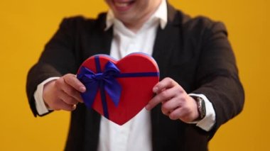 Close up of man presenting St.Valentine's Day gift in heart form to women with excited facial expression on studio background. International Women's Day and birthday holiday concept