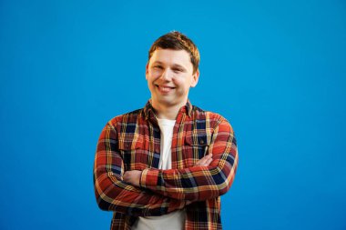 Young handsome man with happy face smiling with crossed arms looking at the camera over blue studio background. Positive person