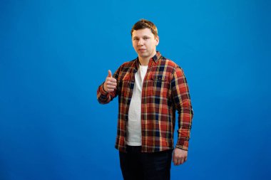 Young handsome man wearing casual shirt over blue background approving doing positive gesture with hand, thumbs up smiling and happy for success. Winner gesture.