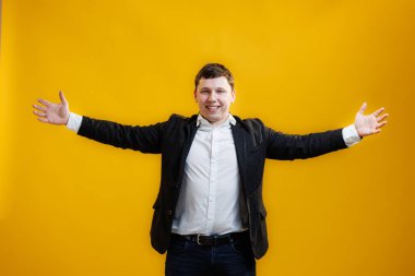 Handsome businessman standing with wide raised arms and welcoming or sharing, wearing official style suit on blue studio background. Wide open hug. Nice to meet you
