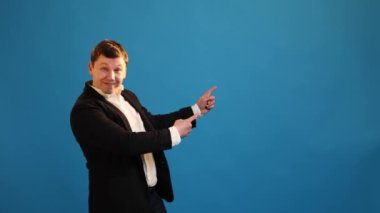 Handsome businessman pointing empty place and showing thumbs up on blue studio background. Advertising area for commercial text, copy space for goods promotion. Look here! Wow, attention at advertise!