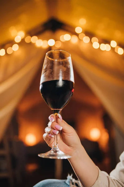 Close up of Woman freelancer drinking wine sitting in cozy glamping tent in autumn evening. Luxury camping tent for outdoor holiday and vacation. Lifestyle concept