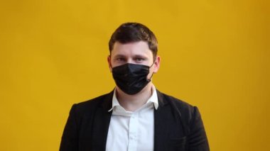 European businessman is wearing protective medical mask on his face and shakes his head NO on yellow studio background. Healthcare and coronavirus protection concept. Covid-19 epidemic