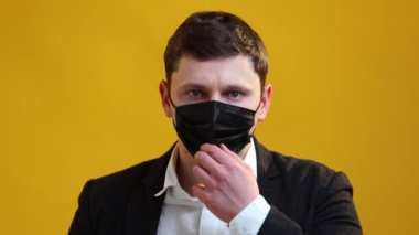 European businessman is takes off protective medical mask from his face and smiling on yellow studio background. Healthcare and coronavirus protection concept. Covid-19 epidemic