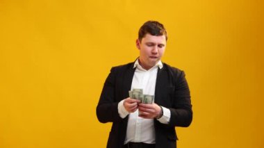 Satisfied businessman counting money. Young happy man calculating cash dollars on yellow studio background. Finance and richness concept