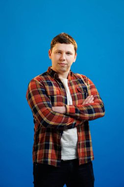 Young handsome man with happy face smiling with crossed arms looking at the camera over blue studio background. Positive person