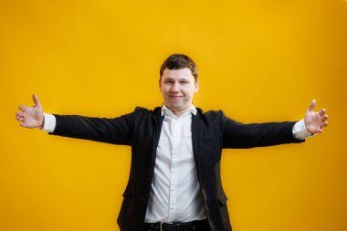 Handsome businessman standing with wide raised arms and welcoming or sharing, wearing official style suit on blue studio background. Wide open hug. Nice to meet you
