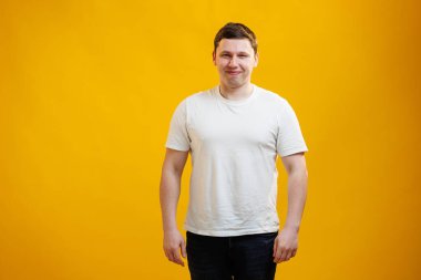 Young handsome man wearing white t-shirt with happy face smiling and looking at the camera over yellow studio background. Positive person