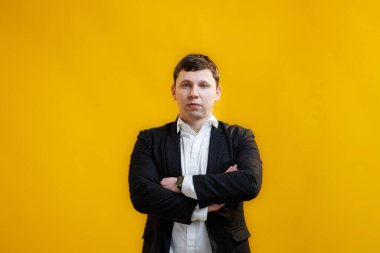 Portrait of handsome businessman with crossing hands standing on yellow studio background and looking at camera