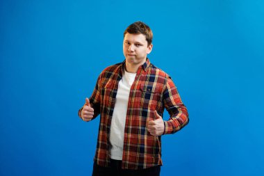 Young handsome man wearing casual shirt over blue background approving doing positive gesture with hand, thumbs up smiling and happy for success. Winner gesture.