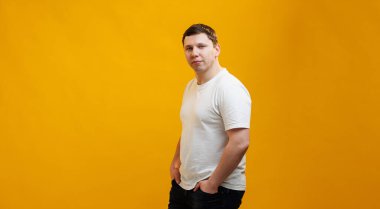 Young handsome man wearing white t-shirt looking at the camera over yellow studio background 