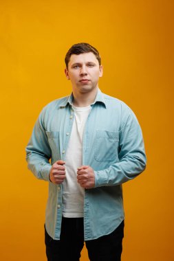 Portrait of handsome european man in shirt looking at camera standing on yellow studio background