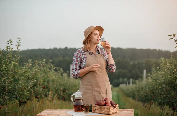 秋天收获的时候 站在果园花园的农民女工在杯子里喝着美味的苹果汁 她笑得很开心 收获时间 — 图库照片