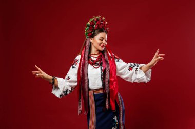 Portrait of ukrainian woman in traditional ethnic clothing and floral red wreath on viva magenta studio background. Ukrainian national embroidered dress call vyshyvanka. Pray for Ukraine