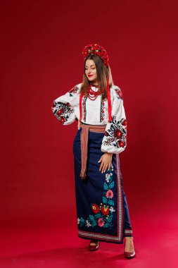 Portrait of ukrainian woman in traditional ethnic clothing and floral red wreath on viva magenta studio background. Ukrainian national embroidered dress call vyshyvanka. Pray for Ukraine