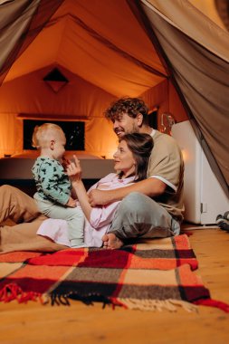 Güzel bebekleri olan mutlu bir aile yaz akşamları glamping 'de birlikte vakit geçiriyorlar. Açık hava eğlencesi ve dinlenme için lüks kamp çadırı. Yaşam tarzı kavramı