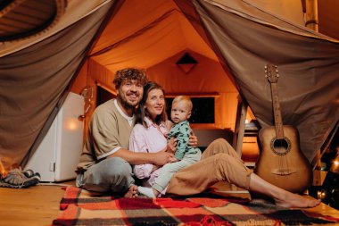 Güzel bebekleri olan mutlu bir aile yaz akşamları glamping 'de birlikte vakit geçiriyorlar. Açık hava eğlencesi ve dinlenme için lüks kamp çadırı. Yaşam tarzı kavramı