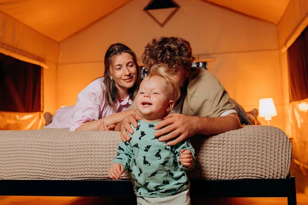 Mutlu bir aile ve güzel bir bebek birlikte oynuyorlar ve yaz akşamları rahat bir şekilde yatakta uzanarak vakit geçiriyorlar. Dışarıda dinlenmek ve dinlenmek için lüks kamp çadırı.