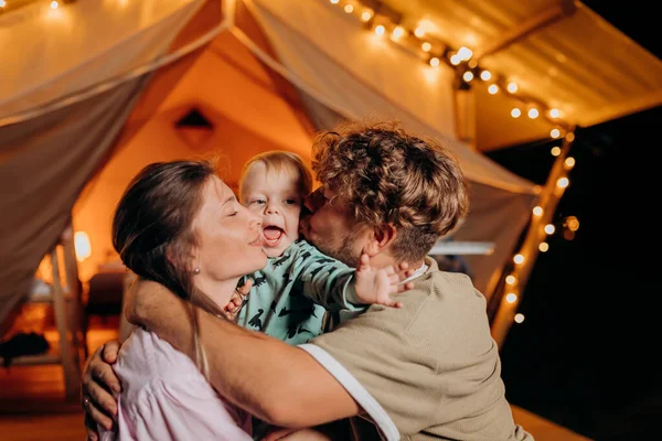 Mutlu bir aile, güzel bir bebeği rahatlatıyor ve yaz akşamları birlikte glamping yaparak sıcacık şenlik ateşinin yanında vakit geçiriyorlar. Açık hava eğlencesi ve dinlenme için lüks kamp çadırı. Yaşam tarzı kavramı