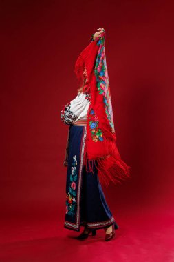 Portrait of ukrainian woman in traditional ethnic clothing and floral red wreath on viva magenta studio background twirls a handkerchief. Ukrainian national embroidered dress call vyshyvanka