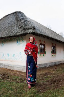 Geleneksel Ukrayna mendili, kolye ve süslü bir barakanın arkasında dikilen işlemeli elbiseli alımlı kadın. Ukrayna, tarz, halk, etnik kültür