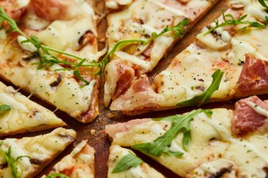 Domatesli, soslu ve otlu ahşap zemin üzerinde servis edilen jambonlu, rukkola ve mantarlı taze pişmiş pizza. Yemek teslimatı konsepti. Restoran menüsü