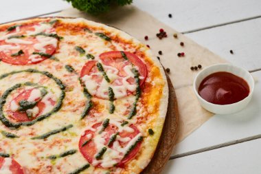 Domatesli taze pişmiş pizza Margarita, sos sosu ve Mozzarella ahşap arka planda soslar ve otlarla servis edilir. Yemek teslimatı konsepti. Restoran menüsü