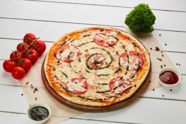 Domatesli taze pişmiş pizza Margarita, sos sosu ve Mozzarella ahşap arka planda soslar ve otlarla servis edilir. Yemek teslimatı konsepti. Restoran menüsü