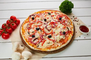 Domates, mantar, kırmızı biber, zeytin, soğan ve Mozzarella ile taze pişmiş vejetaryen pizzası ahşap arka planda sos ve otlarla servis ediliyor. Yemek teslimatı konsepti. Restoran menüsü