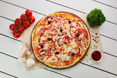 Domates, mantar, kırmızı biber, zeytin, soğan ve Mozzarella ile taze pişmiş vejetaryen pizzası ahşap arka planda sos ve otlarla servis ediliyor. Yemek teslimatı konsepti. Restoran menüsü