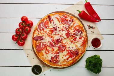 Taze pişmiş sosisli pizza, kırmızı biber ve domatesler ahşap zemin üzerinde sos ve bitkilerle servis ediliyor. Yemek teslimatı konsepti. Restoran menüsü