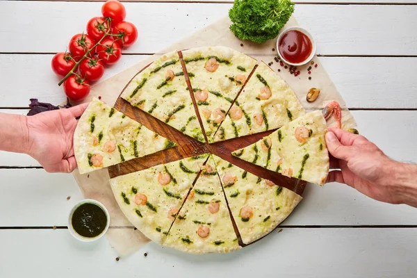 The human hand takes Freshly baked tasty pizza with shrimps and mozzarella cheese served on wooden background with tomatoes, sauce and herbs. Food delivery concept. Restaurant menu