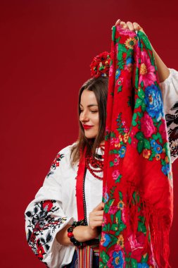 Portrait of ukrainian woman in traditional ethnic clothing and floral red wreath with handkerchief on viva magenta studio background. Ukrainian national embroidered dress call vyshyvanka