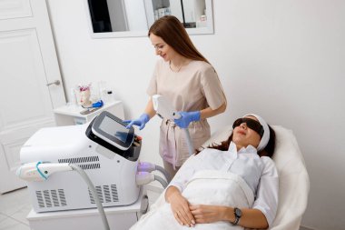 Güzellik uzmanı yüz ve cilt gerdirme işlemi ve saç aldırma için ultrason cihazı tutuyor. Genç kadın kozmetolog klinikte modern kozmetoloji ekipmanları kullanıyor..