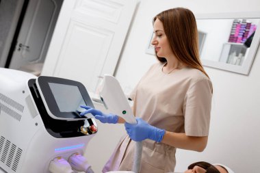 Güzellik uzmanı yüz ve cilt gerdirme işlemi ve saç aldırma için ultrason cihazı tutuyor. Genç kadın kozmetolog klinikte modern kozmetoloji ekipmanları kullanıyor..