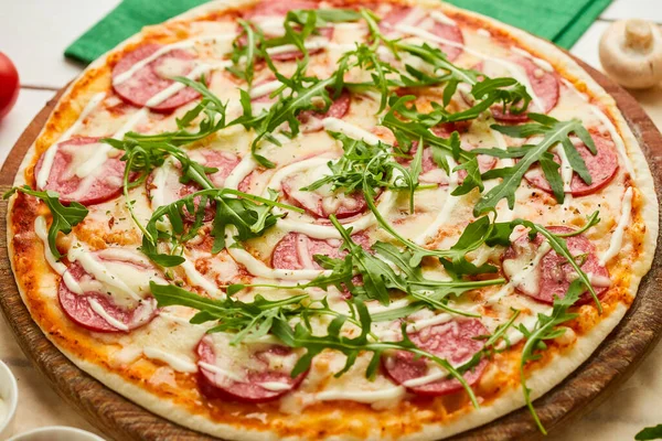 Salamlı, mozzarella peynirli ve rukkola ahşap arka planda domates, sos ve otlarla servis edilen taze pişmiş lezzetli pepperoni pizzası. Yemek teslimatı konsepti. Restoran menüsü