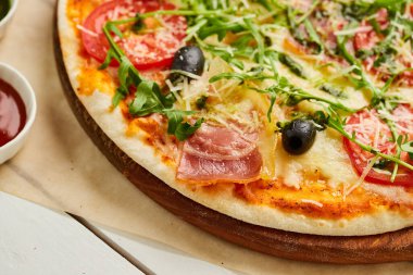 Jambonlu, rukkola soslu, ahşap zemin üzerinde servis edilen zeytinli, domatesli, soslu ve şifalı taze pizza. Yemek teslimatı konsepti. Restoran menüsü