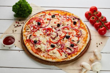 Domates, mantar, kırmızı biber, zeytin, soğan ve Mozzarella ile taze pişmiş vejetaryen pizzası ahşap arka planda sos ve otlarla servis ediliyor. Yemek teslimatı konsepti. Restoran menüsü