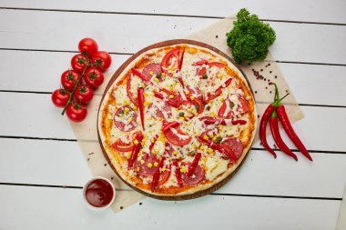 Salamlı, mozzarella peynirli, mısır ve biberli taze pişmiş pepperoni pizza ahşap arka planda domates, sos ve bitkilerle servis ediliyor. Yemek teslimatı konsepti. Restoran menüsü