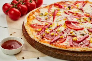 Salamlı, mozzarella peynirli, mısır ve biberli taze pişmiş pepperoni pizza ahşap arka planda domates, sos ve bitkilerle servis ediliyor. Yemek teslimatı konsepti. Restoran menüsü