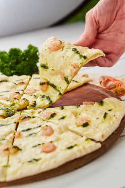 İnsan eli, ahşap arka planda domates, sos ve otlarla servis edilen karides ve mozzarella peynirli taze pişmiş lezzetli pizzayı alır. Yemek teslimatı konsepti. Restoran menüsü