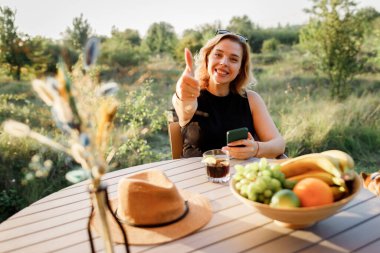 Mutlu Kadın Serbest Çalışan, güneşli bir günde rahat bir glamping çadırında dinlenirken telefonla içki içiyor. Yaz tatili ve tatil için lüks kamp çadırı. Yaşam tarzı kavramı