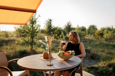 Mutlu Kadın Serbest Çalışan, güneşli bir günde rahat bir glamping çadırında dinlenirken telefonla içki içiyor. Yaz tatili ve tatil için lüks kamp çadırı. Yaşam tarzı kavramı