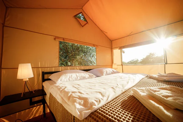 Interior of Cozy open glamping tent with light inside during sunset. Luxury camping tent for outdoor summer holiday and vacation. Lifestyle concept