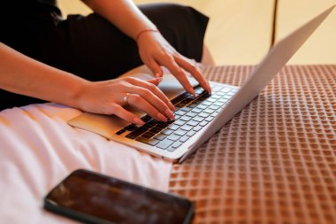 Smiling Woman freelancer using a laptop on a cozy glamping tent in a sunny day. Luxury camping tent for outdoor summer holiday and vacation. Lifestyle concept